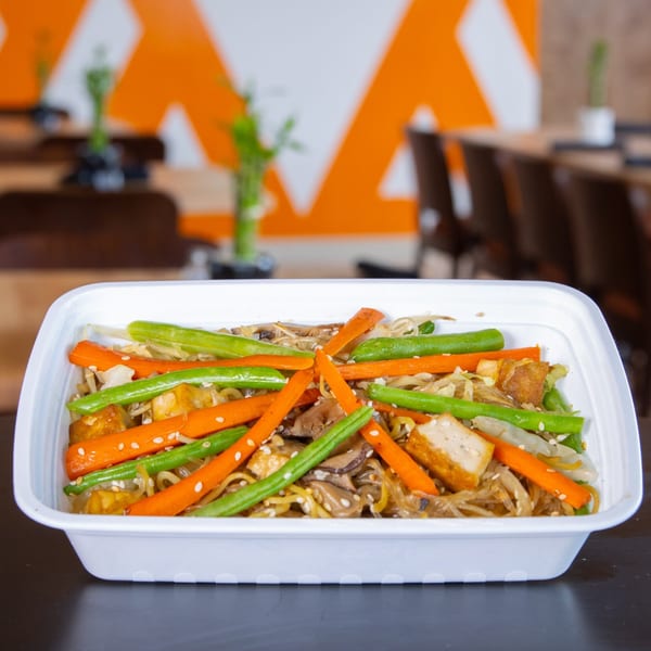 FoodAMed's healthy noodle dish with carrots, green beans, tofu, and sesame seeds in a white container.