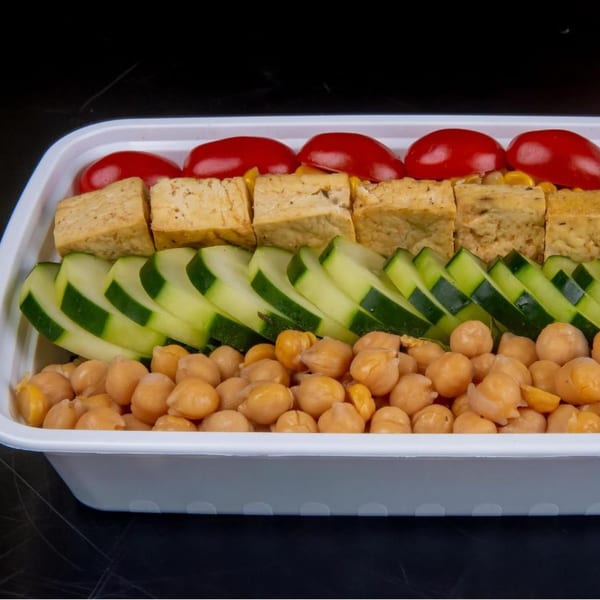 A healthy FoodAMed meal with chickpeas, sliced cucumbers, tofu, and cherry tomatoes in a white container.