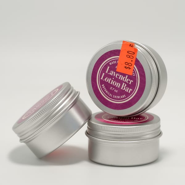 Three round silver tins of "Lavender Lotion Bar Botanical Skincare," one with an orange $8.80 sticker.