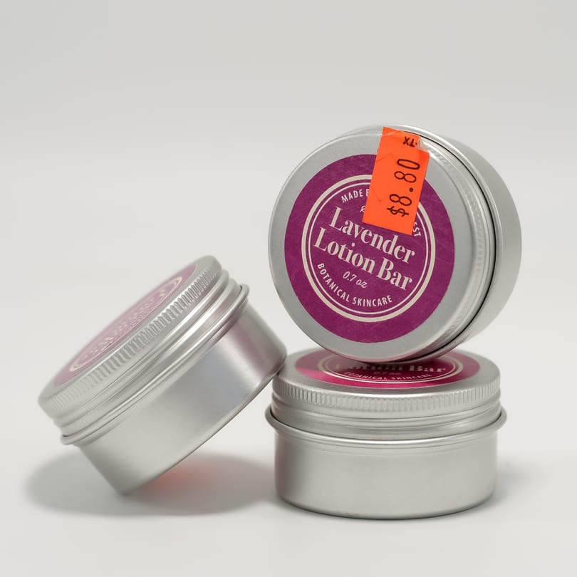 Three round silver tins of "Lavender Lotion Bar Botanical Skincare," one with an orange $8.80 sticker.