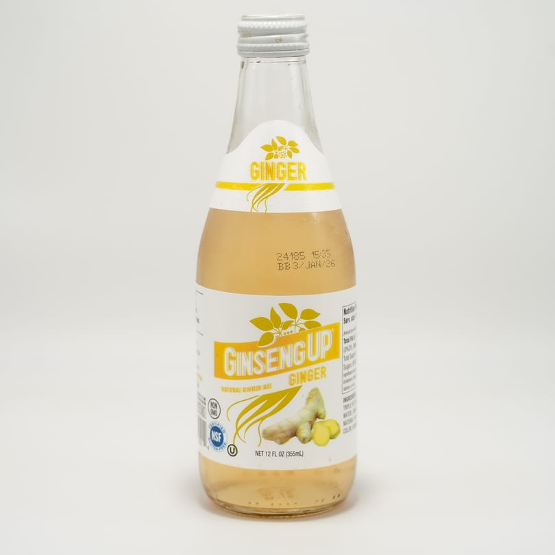 A bottle of Ginseng Up Natural Ginger Ale with a white and yellow label on a white background.