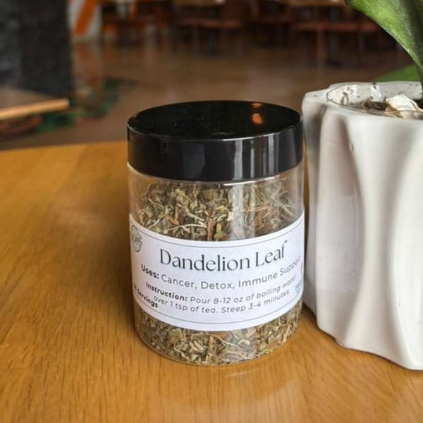 A clear jar of Dandelion Leaf tea with instructions sits on a wooden table next to a plant.