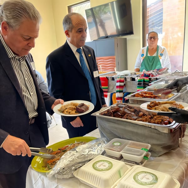 People serving themselves healthy FoodAMed dishes from a buffet line with to-go containers.