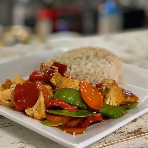 FoodAMed's healthy stir-fry with colorful vegetables, tofu, sesame seeds, and brown rice on a white plate.