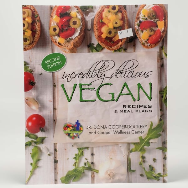 Vegan cookbook cover with bruschetta, tomatoes, garlic, and arugula on a white wooden background.