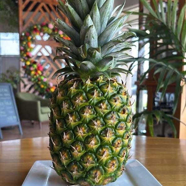 A whole pineapple on a white plate, with a blurred restaurant background.