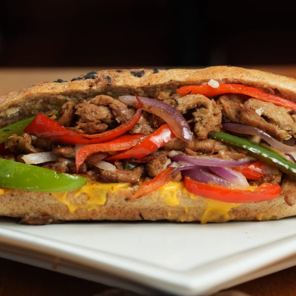 A healthy FoodAMed sandwich with meat, red and green peppers, and onions on a white plate.