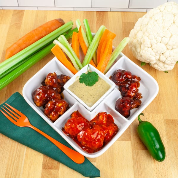 FoodAMed's healthy cauliflower wings in red and brown sauces, with carrot and celery sticks and dip.