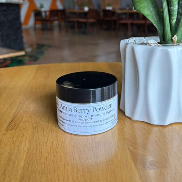 A small white jar of Amla Berry Powder on a wooden table next to a potted plant.