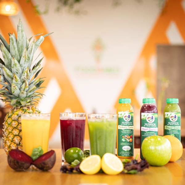 Fresh juices and whole fruits, including pineapple, beets, limes, lemons, green apple, and orange.