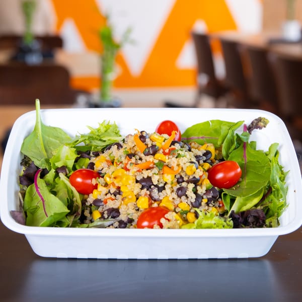 FoodAMed healthy quinoa salad with black beans, corn, and cherry tomatoes in a white container.