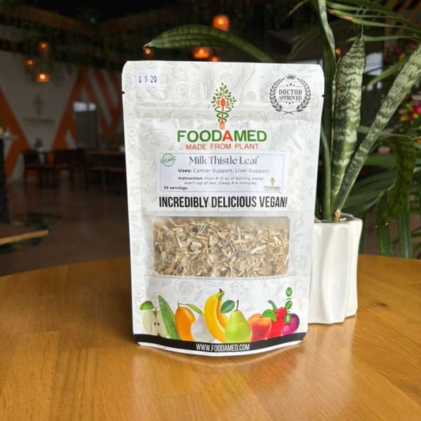 A white Foodamed Milk Thistle Leaf tea bag with fruit illustrations sits on a wooden table.