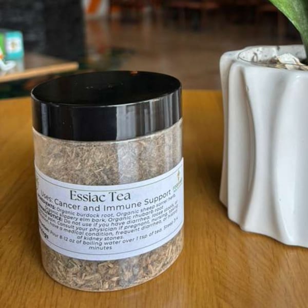 A clear jar of Essiac Tea, labeled for "Cancer and Immune Support," sits on a wooden table.