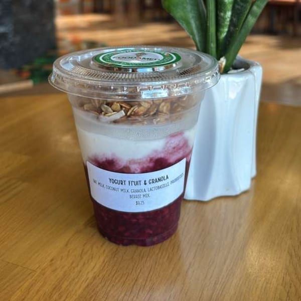 A plastic cup of yogurt parfait with berries, granola, and coconut milk on a wooden table.