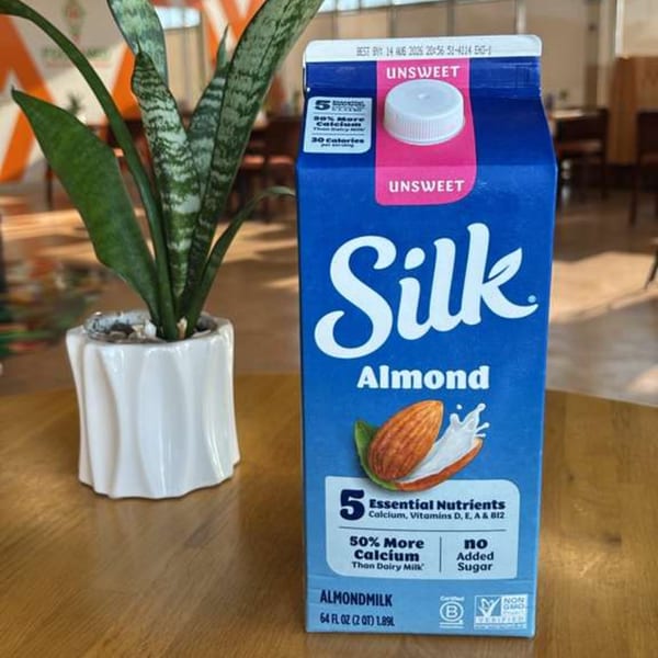 A carton of Silk Unsweet Almondmilk stands next to a potted snake plant on a wooden table.