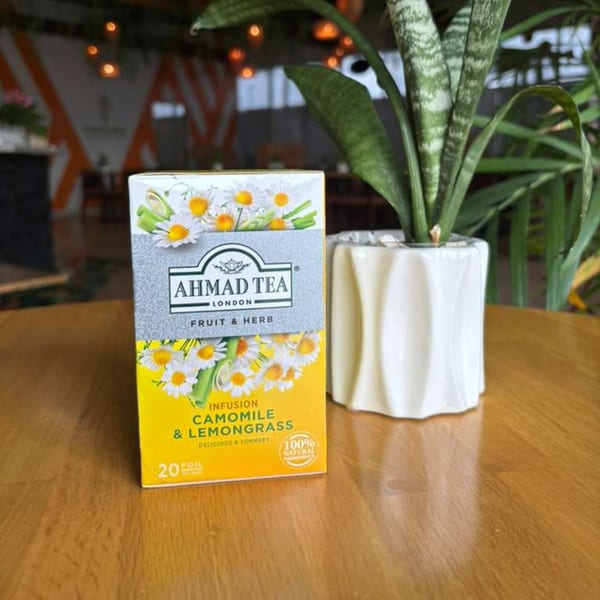Ahmad Tea London Chamomile & Lemongrass tea box next to a potted plant on a wooden table.