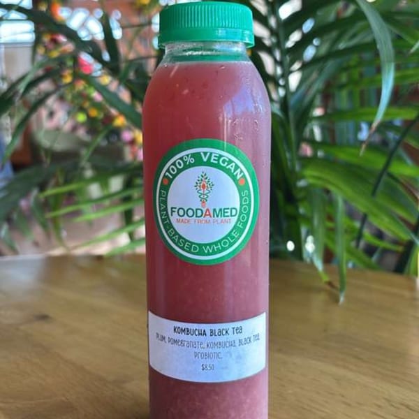 A bottle of Foodamed Plum Pomegranate Kombucha Black Tea with a green cap on a wooden table.