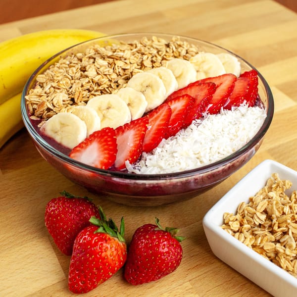 A FoodAMed acai bowl with granola, banana slices, strawberries, and shredded coconut.