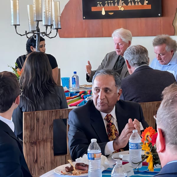 Diners, including a man in a suit and tie, seated at a table with water bottles and food.