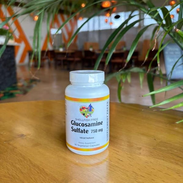 A white bottle of Glucosamine Sulfate 750 mg dietary supplement on a wooden table.
