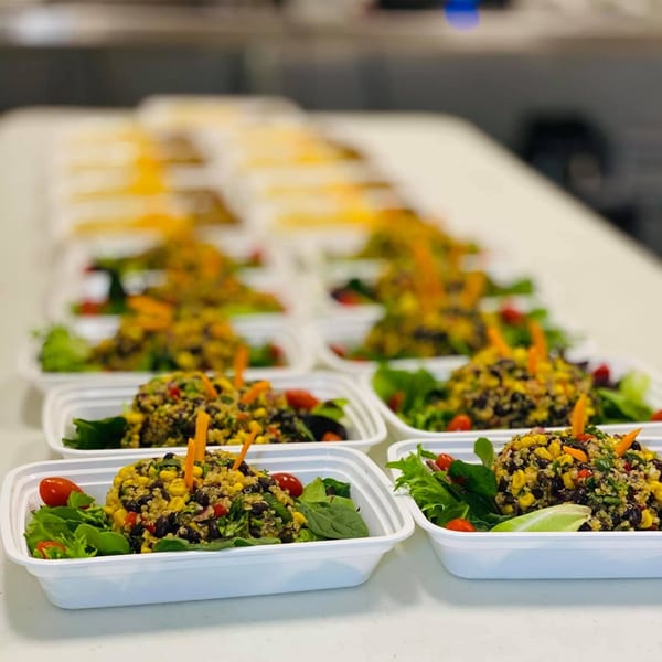 Rows of healthy FoodAMed quinoa, black bean, and corn salads in white to-go containers.