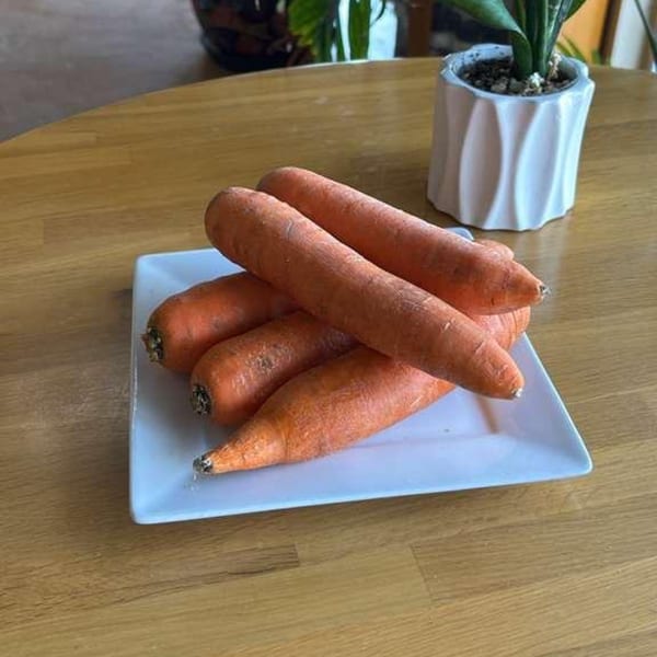 Several fresh, unpeeled carrots are piled on a white rectangular plate on a wooden table.