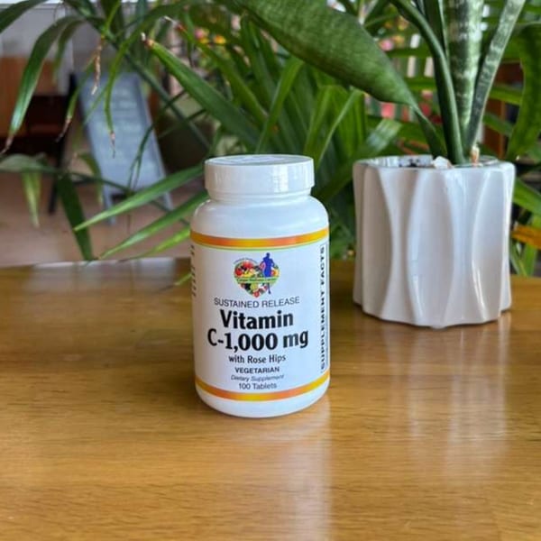 White bottle of Vitamin C-1,000 mg with Rose Hips on a wooden table with plants.