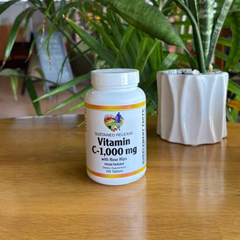 White bottle of Vitamin C-1,000 mg with Rose Hips on a wooden table with plants.