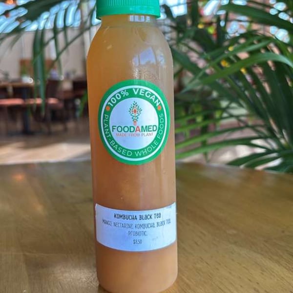 A bottle of Foodamed Mango Nectarine Kombucha Black Tea on a wooden table with plants.