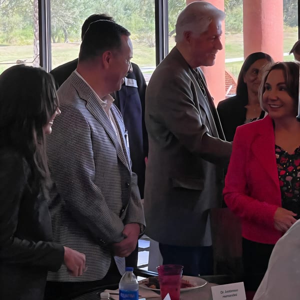 People in business attire are gathered at a FoodAMed event, with a man in a suit shaking hands.