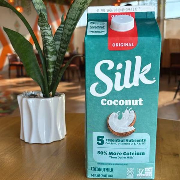A carton of Silk Coconutmilk stands next to a potted snake plant on a wooden table.