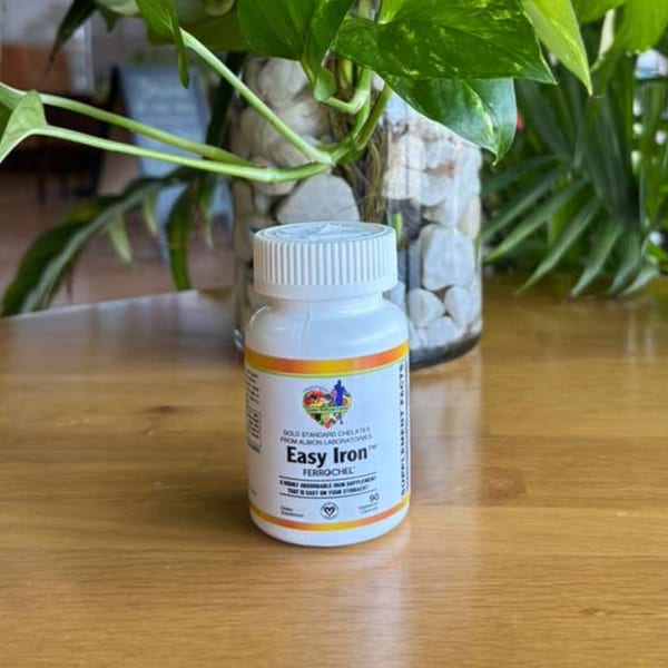 A white bottle of "Easy Iron" supplement on a wooden table, with green plants in the background.