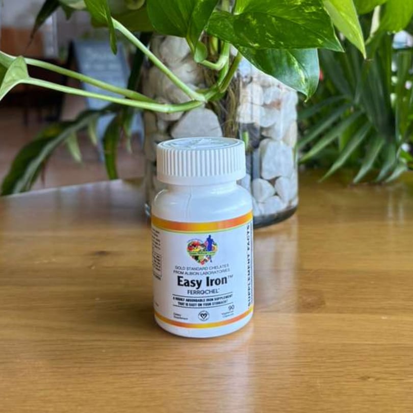 A white bottle of "Easy Iron" supplement on a wooden table, with green plants in the background.