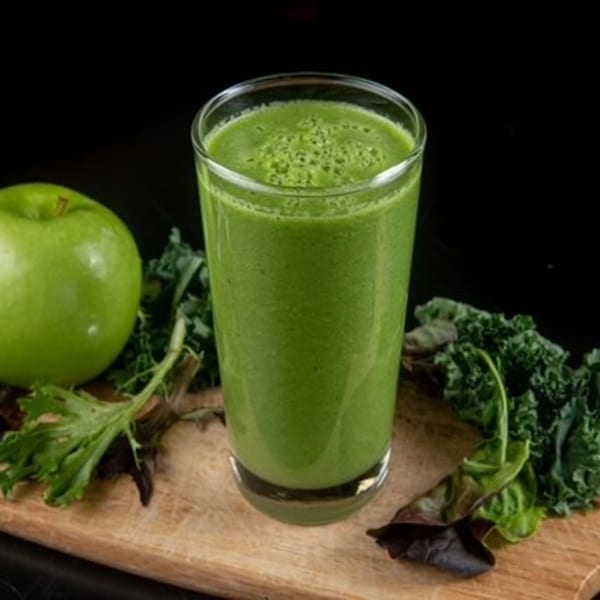 A vibrant green smoothie in a glass, with a green apple and leafy greens on a wooden board.