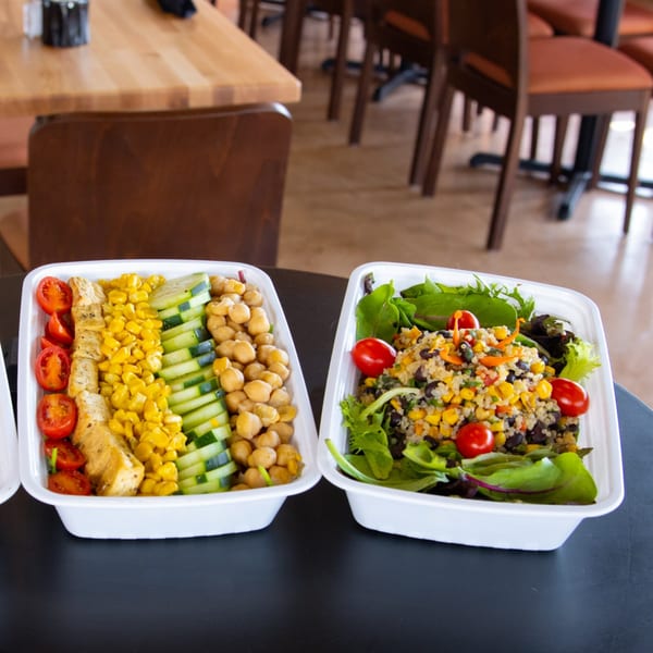 Two healthy FoodAMed meals, one with chicken, corn, cucumber, and chickpeas, the other a quinoa salad.