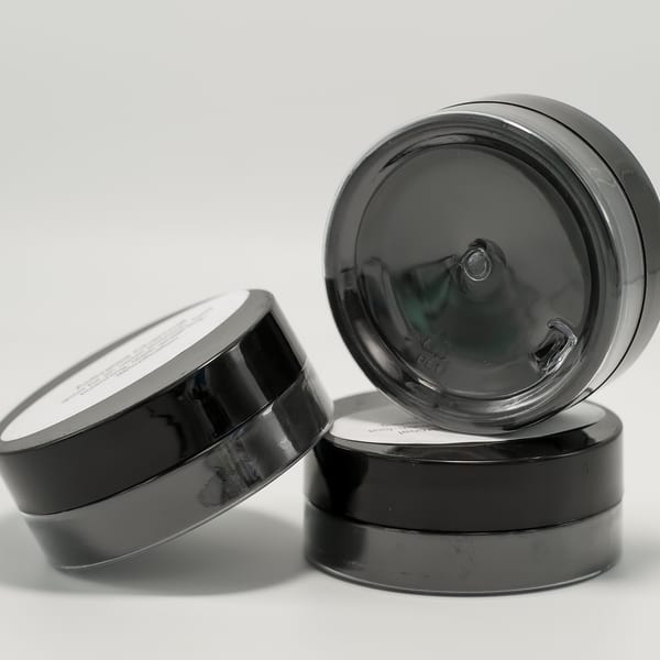 Three dark gray, round containers with white labels are stacked and arranged on a white surface.