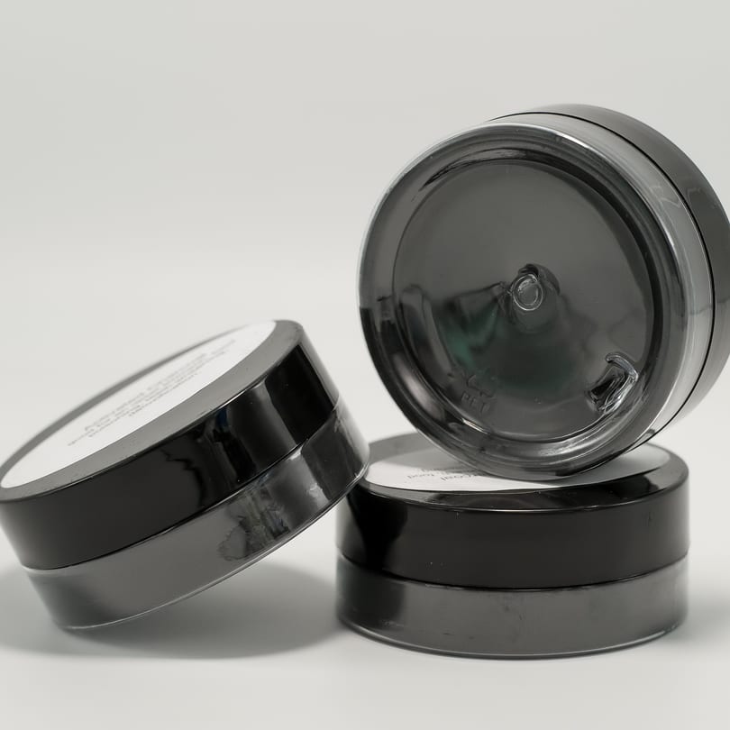 Three dark gray, round containers with white labels are stacked and arranged on a white surface.