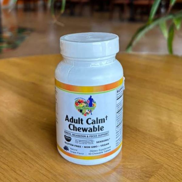 A white bottle of "Adult Calm Chewable" dietary supplements, grape flavor, on a wooden surface.