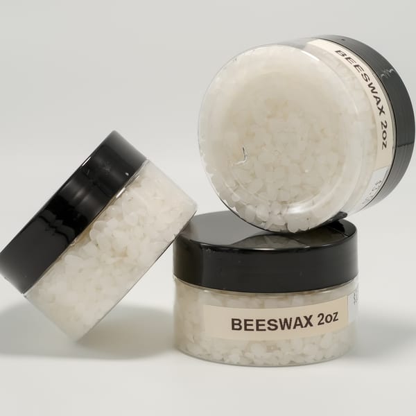 Three clear jars with black lids filled with white beeswax pellets, one jar on its side.