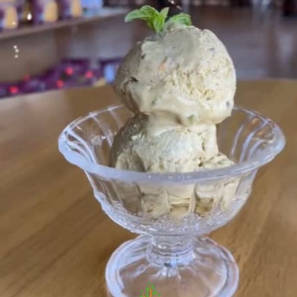 Two scoops of light green ice cream with mint leaves in a clear glass bowl on a wooden table.