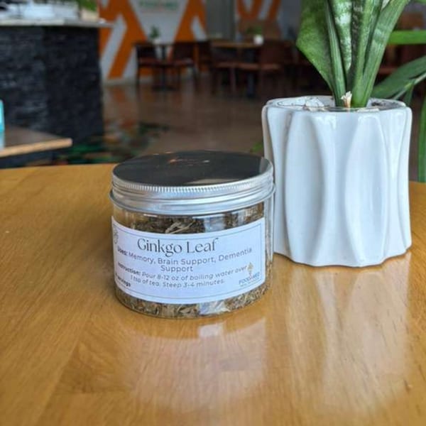 A jar of Ginkgo Leaf tea on a wooden table next to a potted plant.