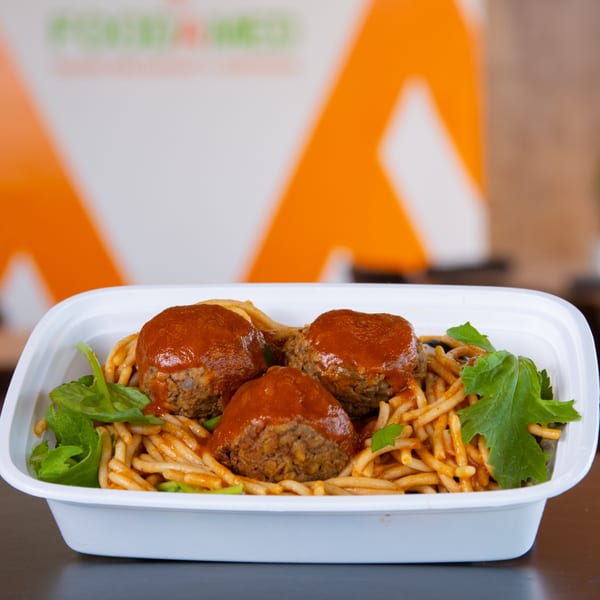 FoodAMed's healthy spaghetti and meatballs with fresh greens in a white to-go container.