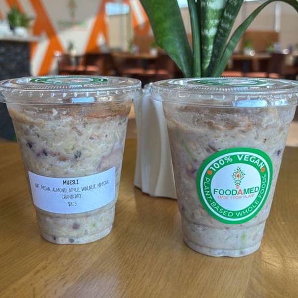 Two clear cups of vegan muesli with oats, pecan, almond, apple, walnut, and cranberry.