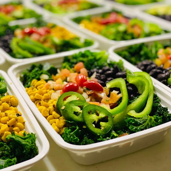 Rows of healthy FoodAMed meal prep containers with kale, corn, black beans, and peppers.