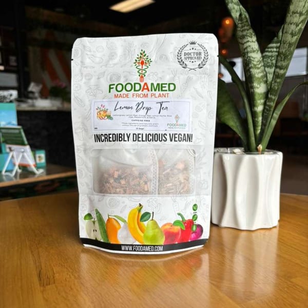 A Foodamed Lemon Drop Tea bag, with fruit illustrations, sits on a wooden table next to a plant.