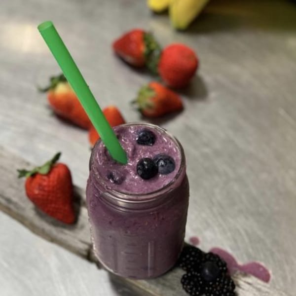 A FoodAMed berry smoothie in a jar with a green straw, surrounded by fresh strawberries and blackberries.
