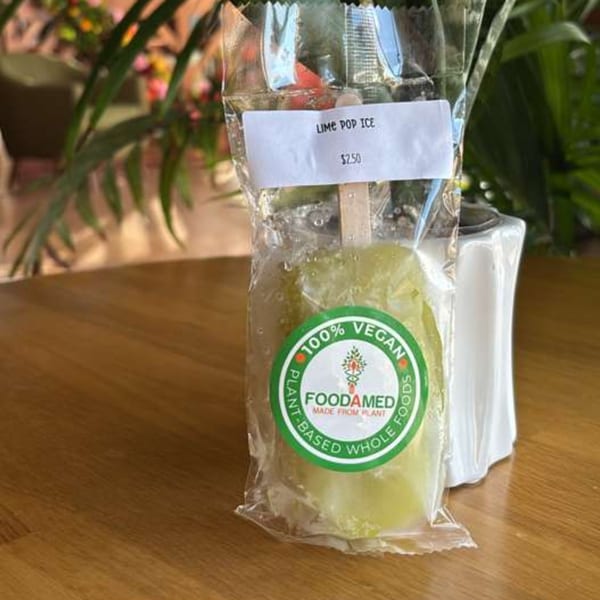 A packaged lime pop ice from Foodamed, 100% vegan, on a wooden table.