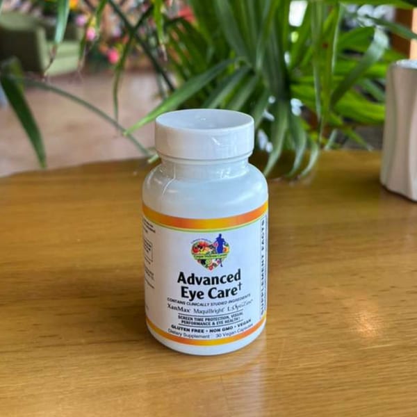 A white bottle of "Advanced Eye Care" dietary supplement on a wooden table with green plants.