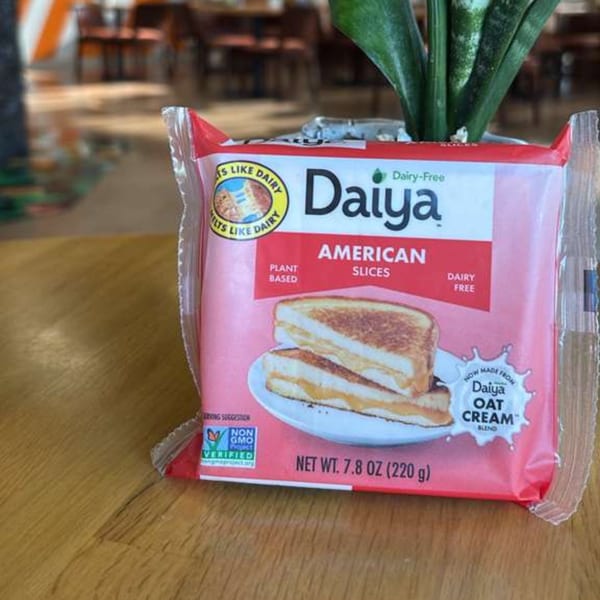 A package of Daiya Dairy-Free American Slices on a wooden table with a plant in the background.