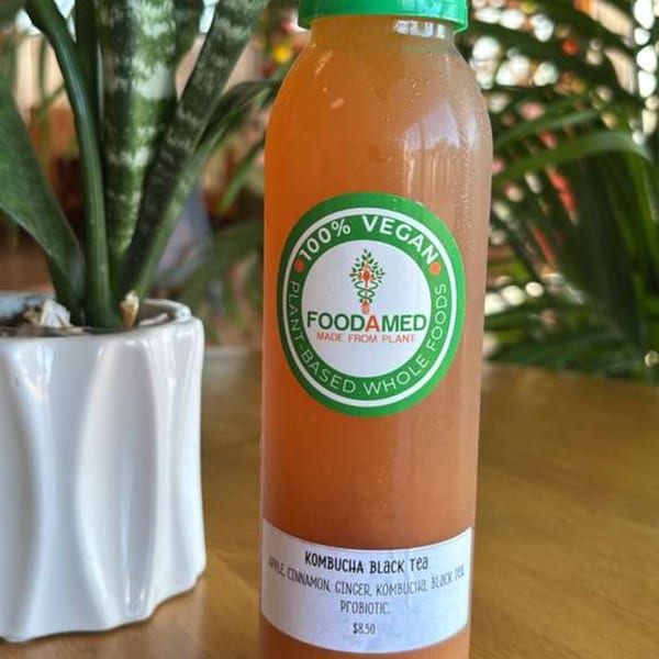 A bottle of Foodamed Kombucha Black Tea, apple cinnamon ginger flavored, with a plant in a white pot.